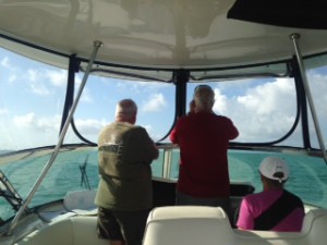 Ann takes a turn at the helm as Cliff scans horizon with binoculars for next day mark.  Gary is on the look out as well!